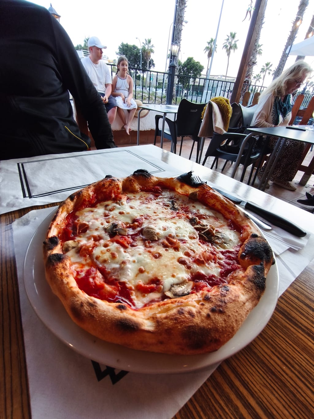 Pizza napolitana en la terraza con palmeras al fondo